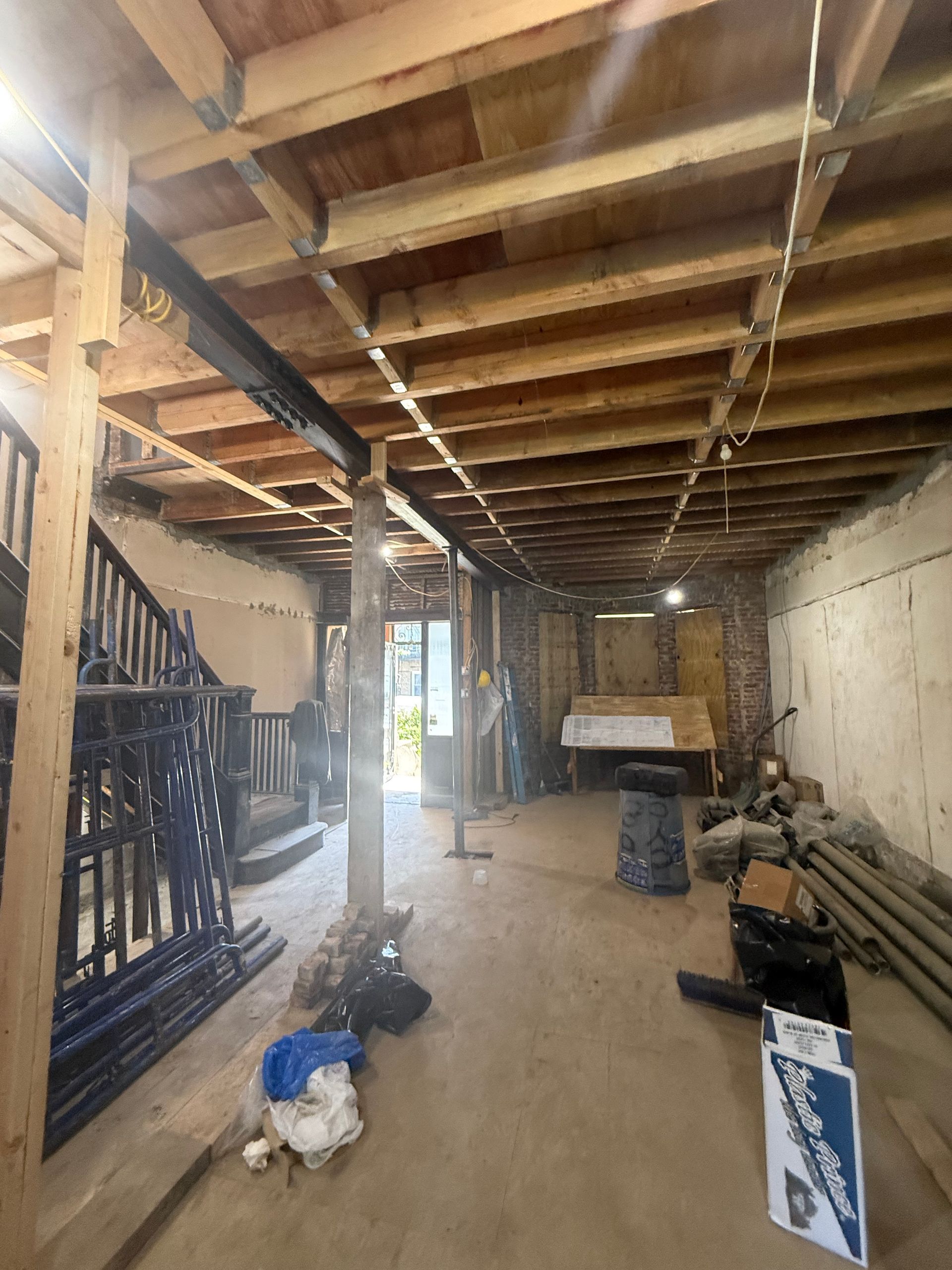 Basement renovation with exposed beams, support posts, and construction materials.