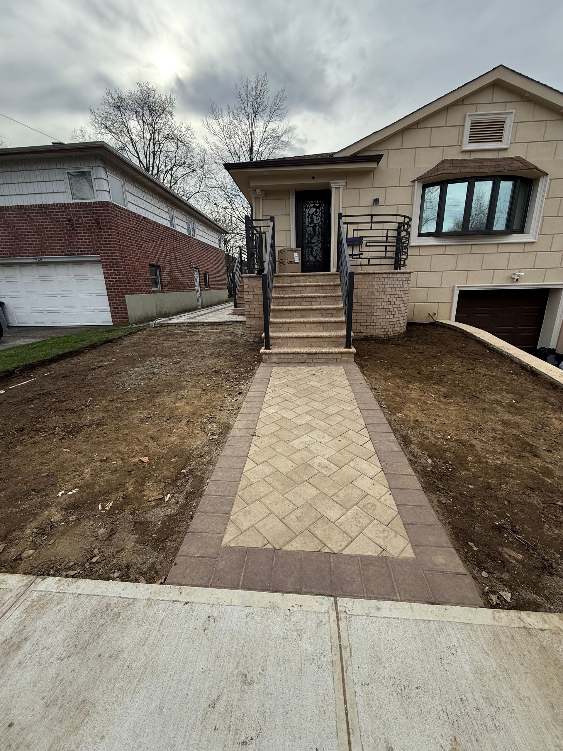 A house with a paver walkway leading to front steps.  Brown, tan, and beige colors.  Overcast sky.