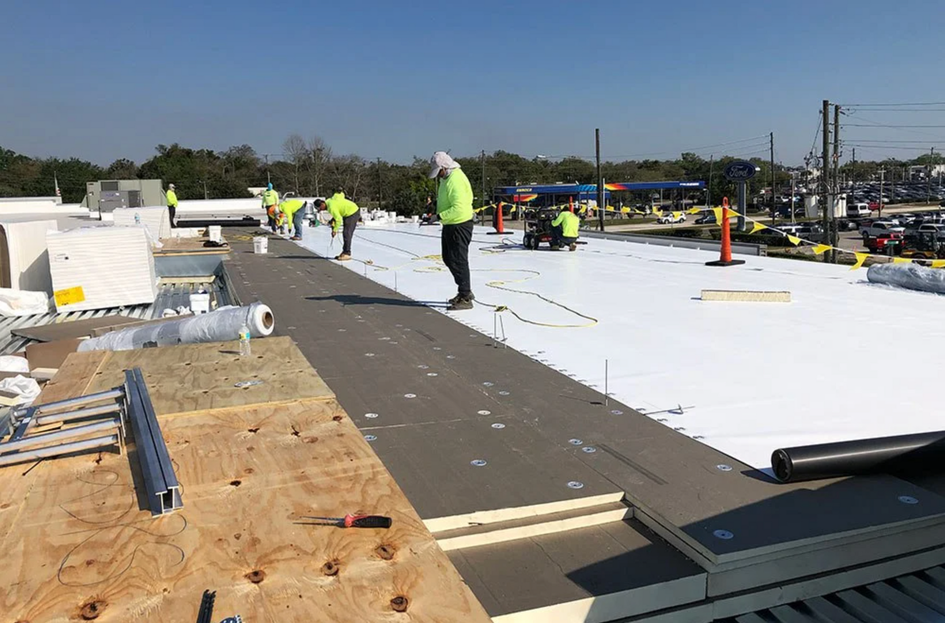Construction workers on a flat roof installing white and gray roofing materials on a sunny day.