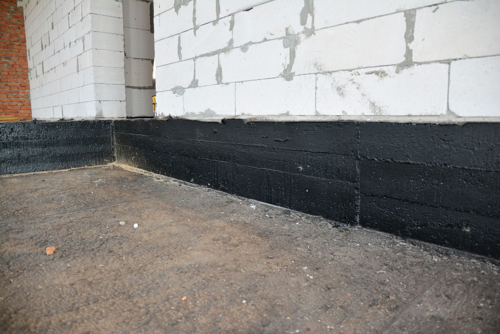 Partially painted white cinder block wall with black waterproofing along the bottom at ground level