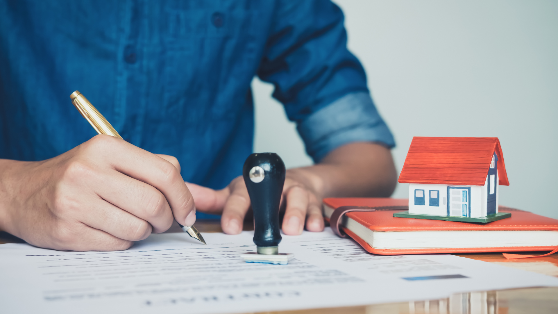 A man is sitting at a table signing a document next to a model house.