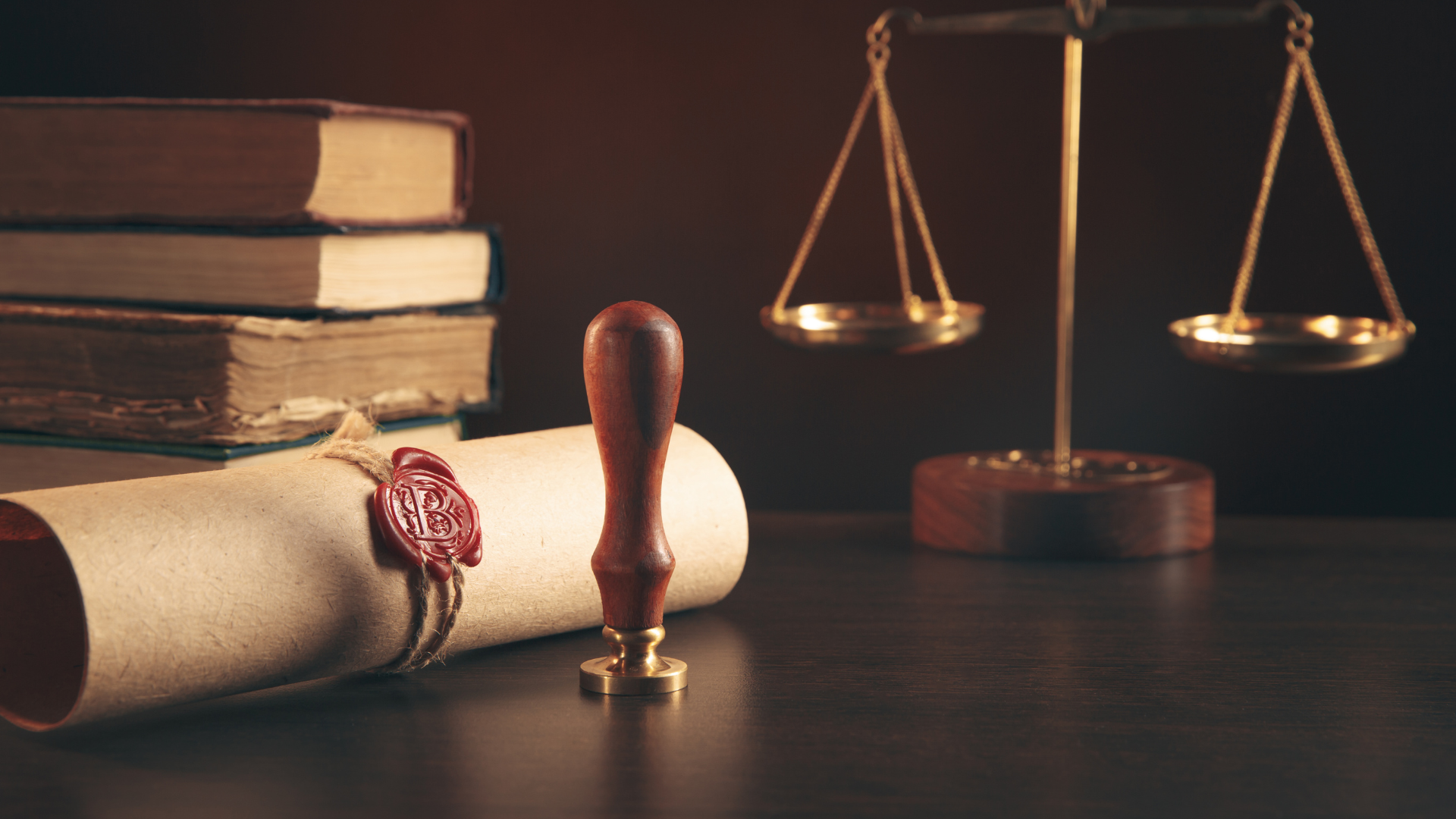 A stack of books , a seal , and a scale of justice on a table.