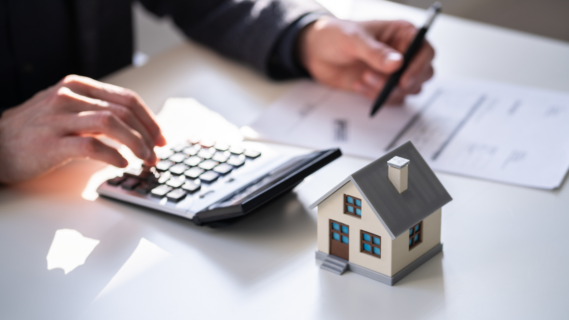 A person is using a calculator next to a model house.