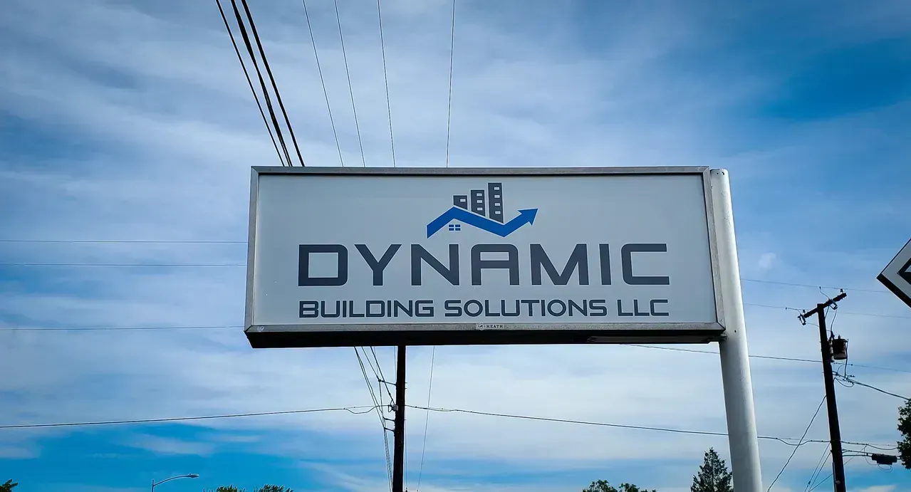 Sign for Dynamic Building Solutions LLC against a blue sky with power lines.
