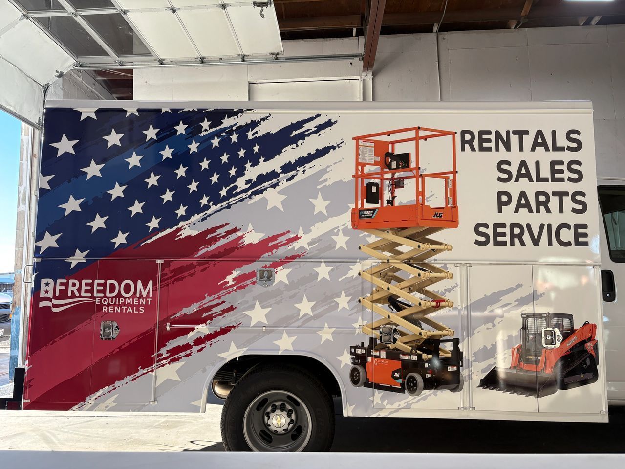 Trailer with American flag graphic, scissor lifts, and text: “Rentals Sales Parts Service.”