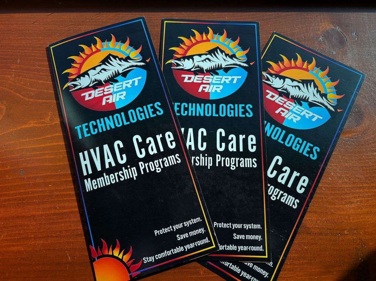 Three Desert Air Technologies HVAC care brochures fanned out on a wooden surface.
