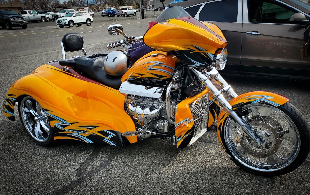 Bright orange custom motorcycle with chrome wheels parked on pavement at a car show