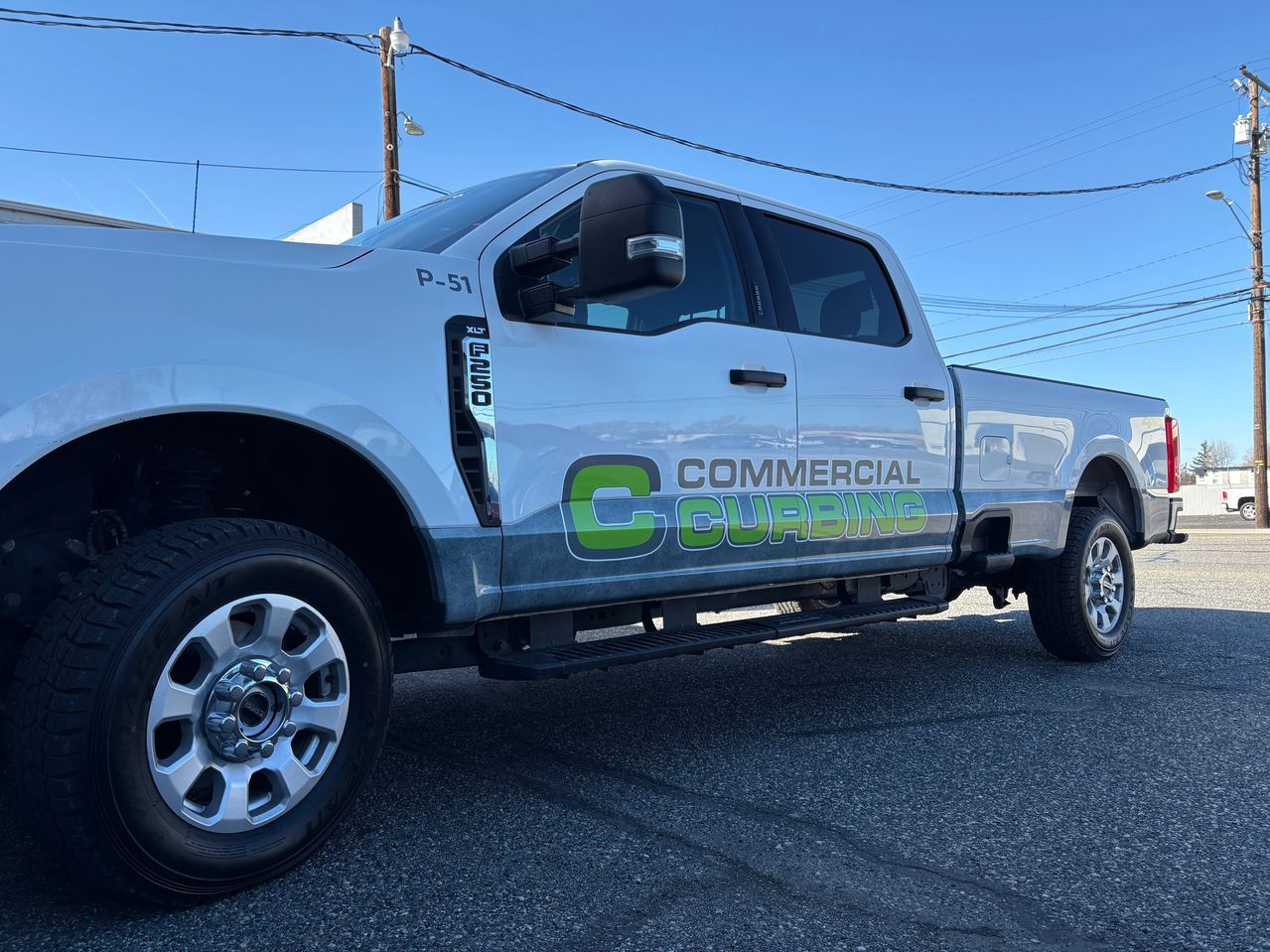 White commercial pickup truck with company logo, parked outdoors on a sunny day