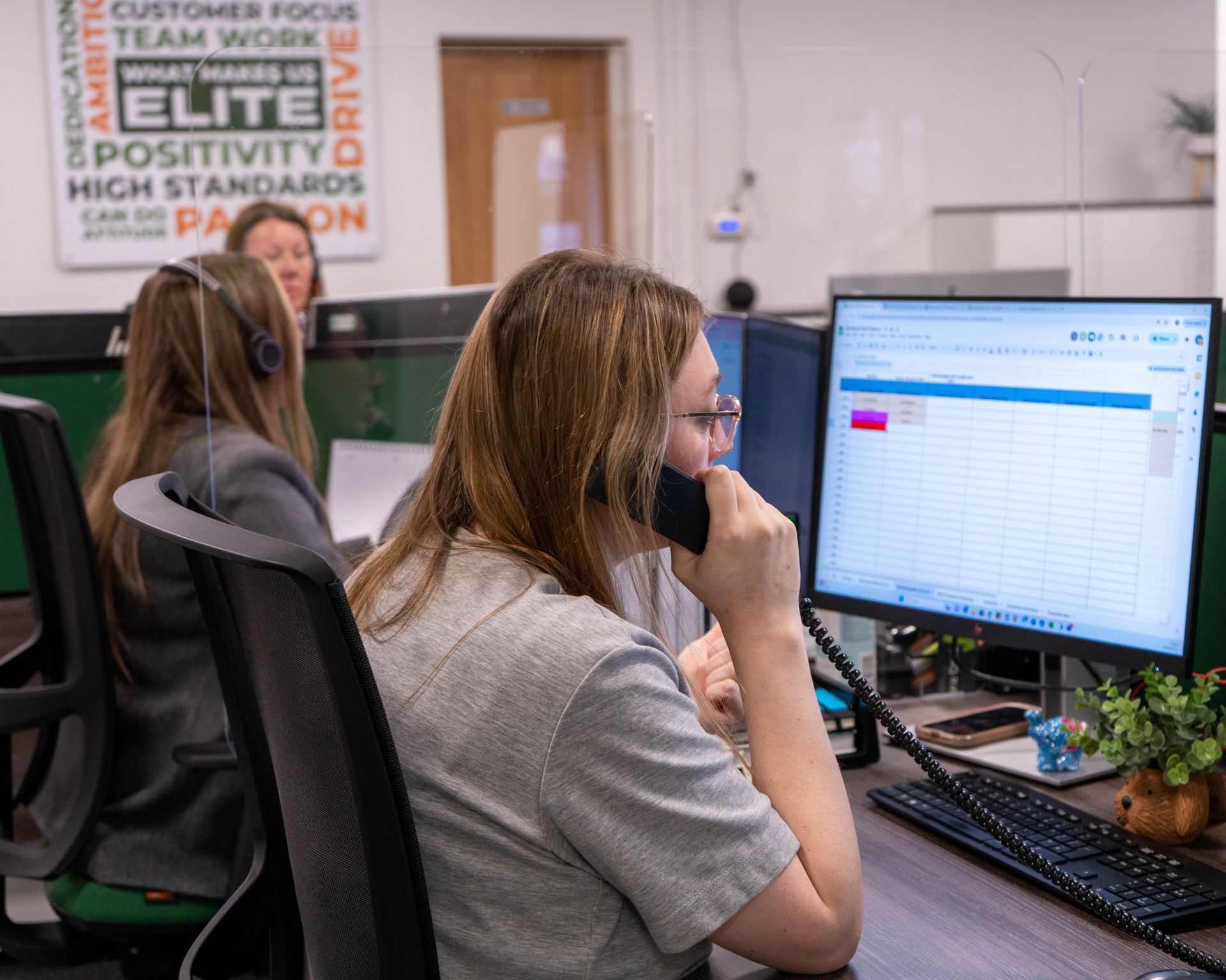 Two people working at computers in an office, one focused on a screen with charts.
