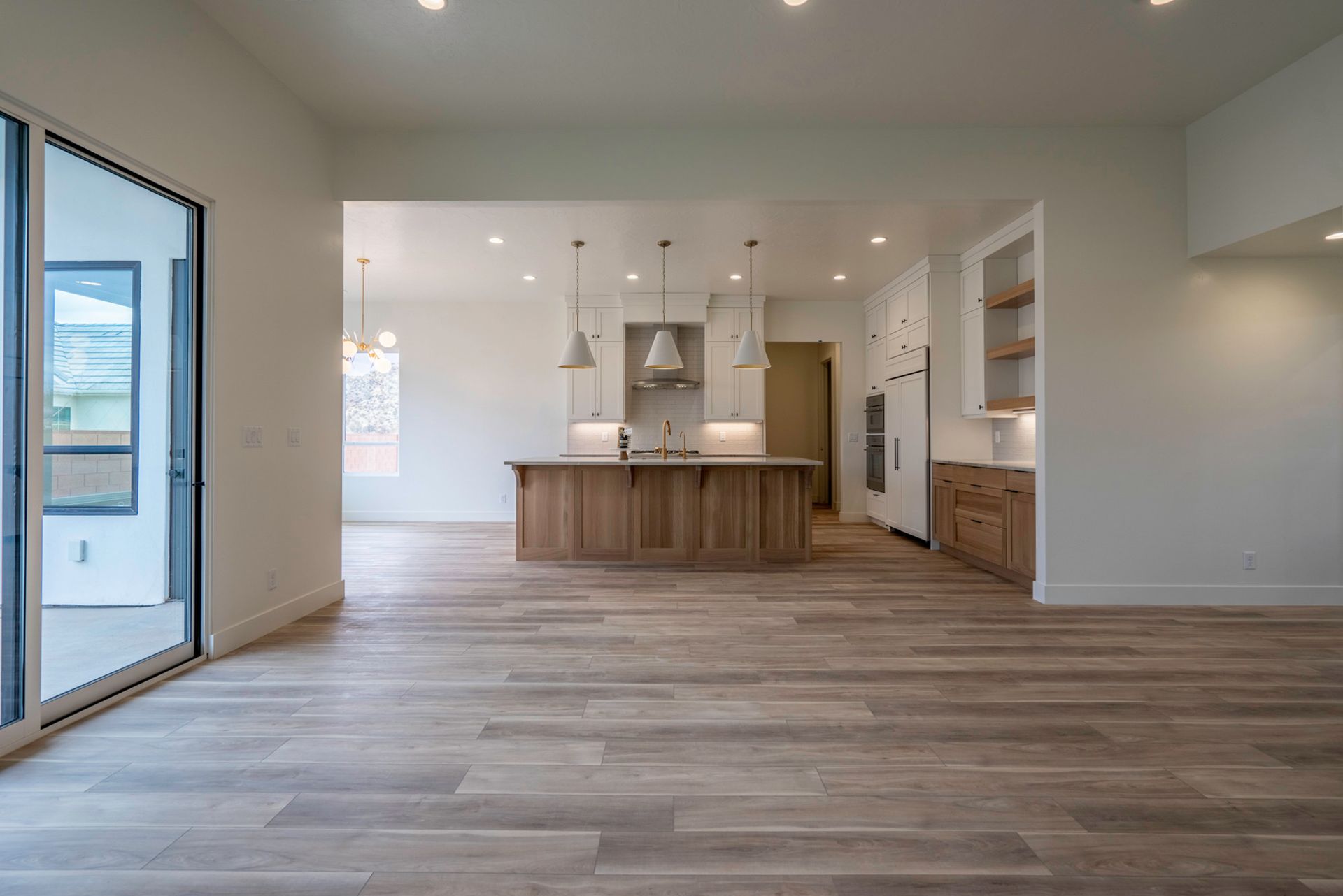 A large empty room with a kitchen and sliding glass doors.