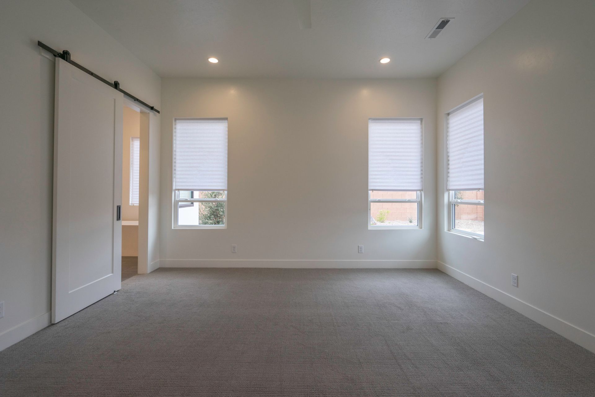 An empty bedroom with a sliding barn door and two windows.