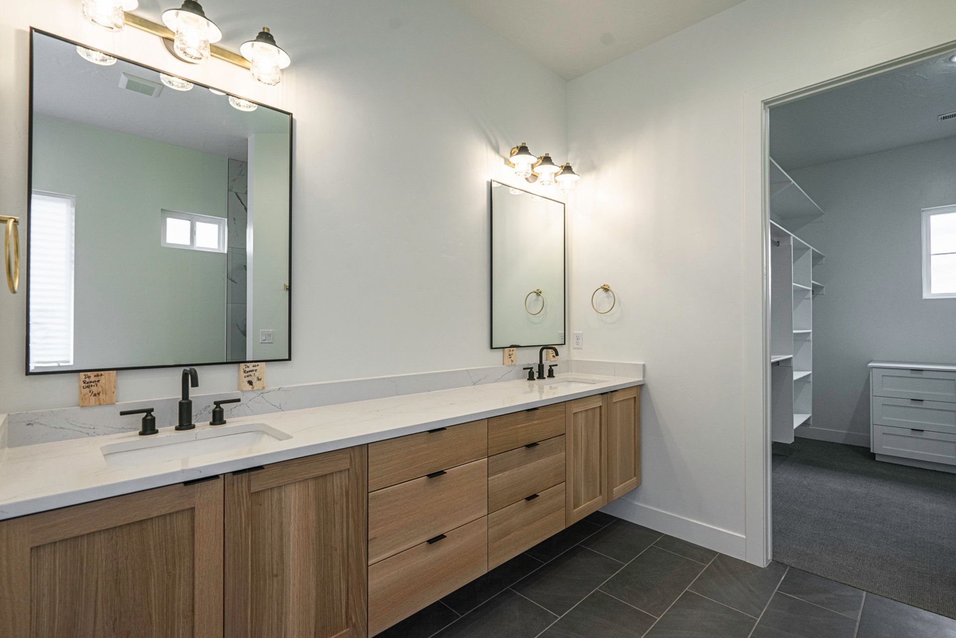 A bathroom with two sinks , two mirrors and a walk in closet.