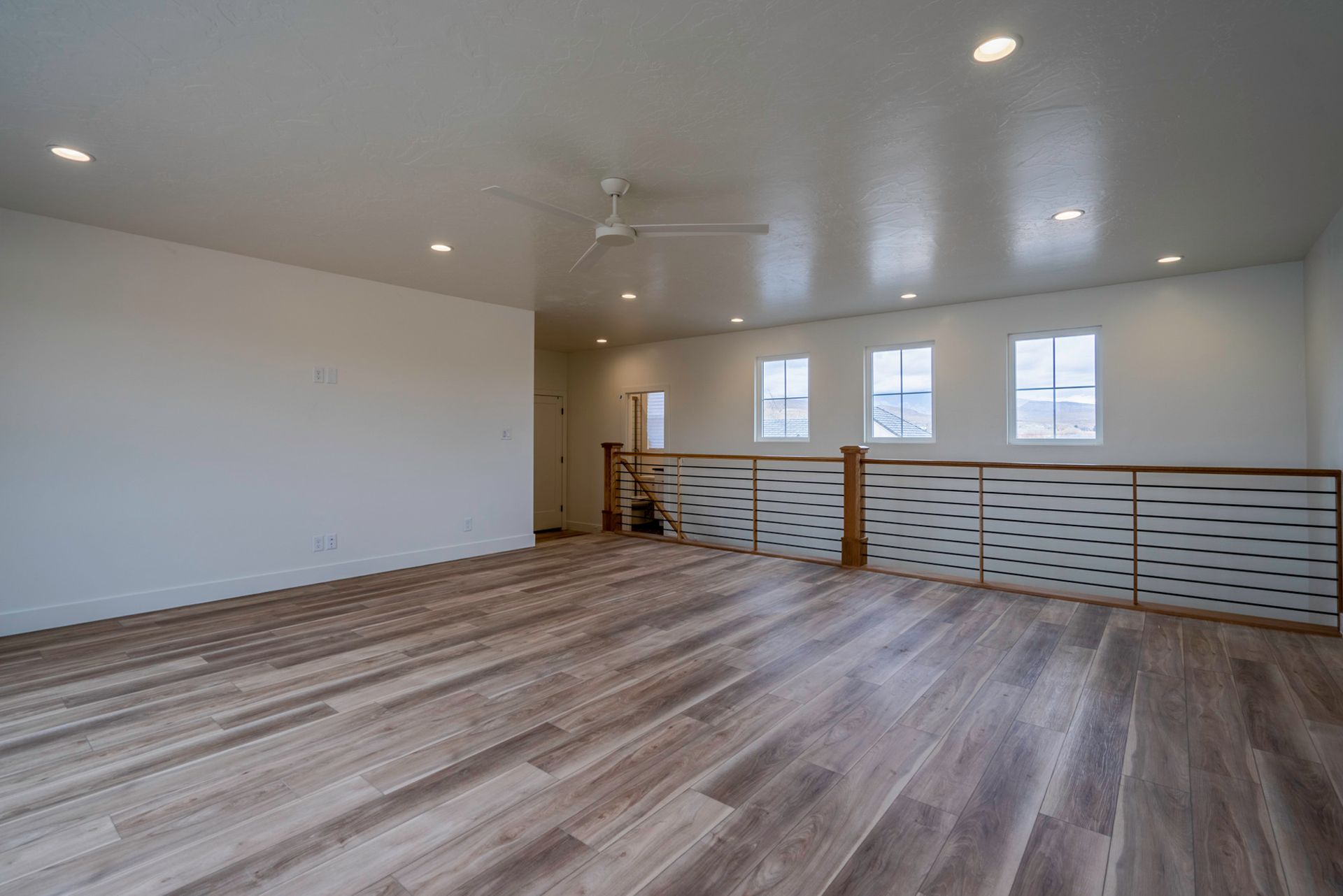 A large empty room with hardwood floors and a ceiling fan.