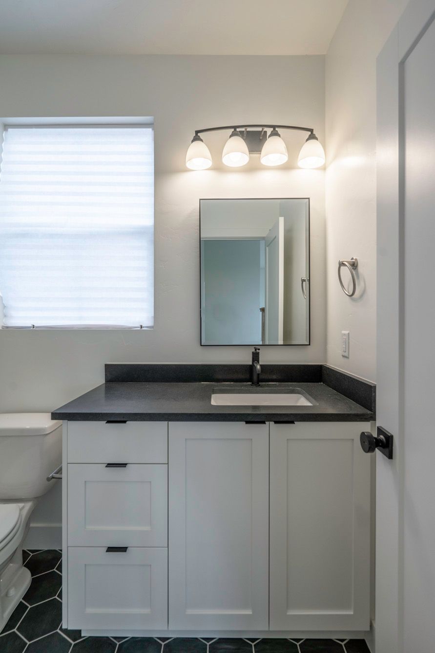 A bathroom with a sink , mirror and window.