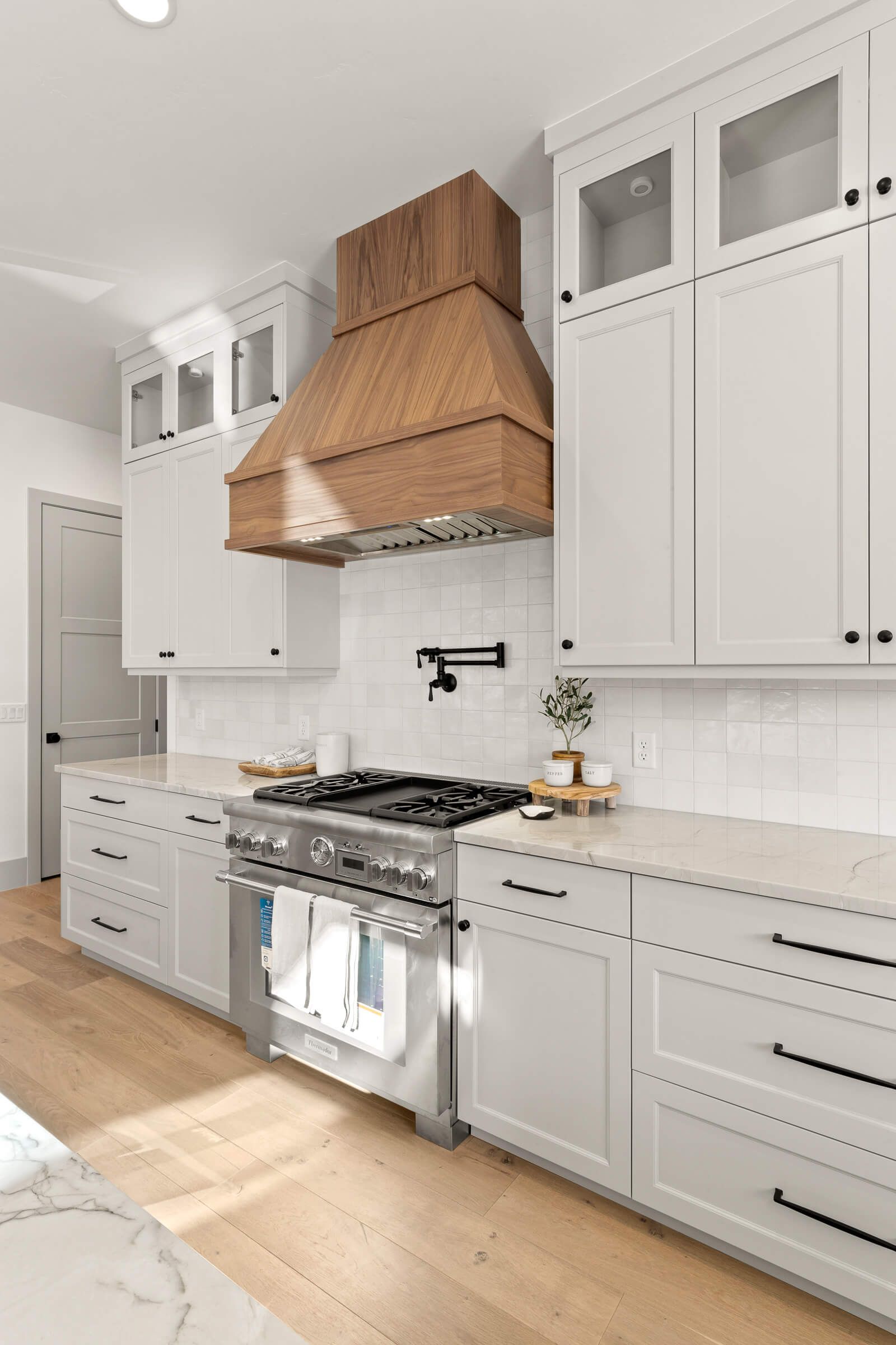 A kitchen with white cabinets , a stove , and a wooden hood.