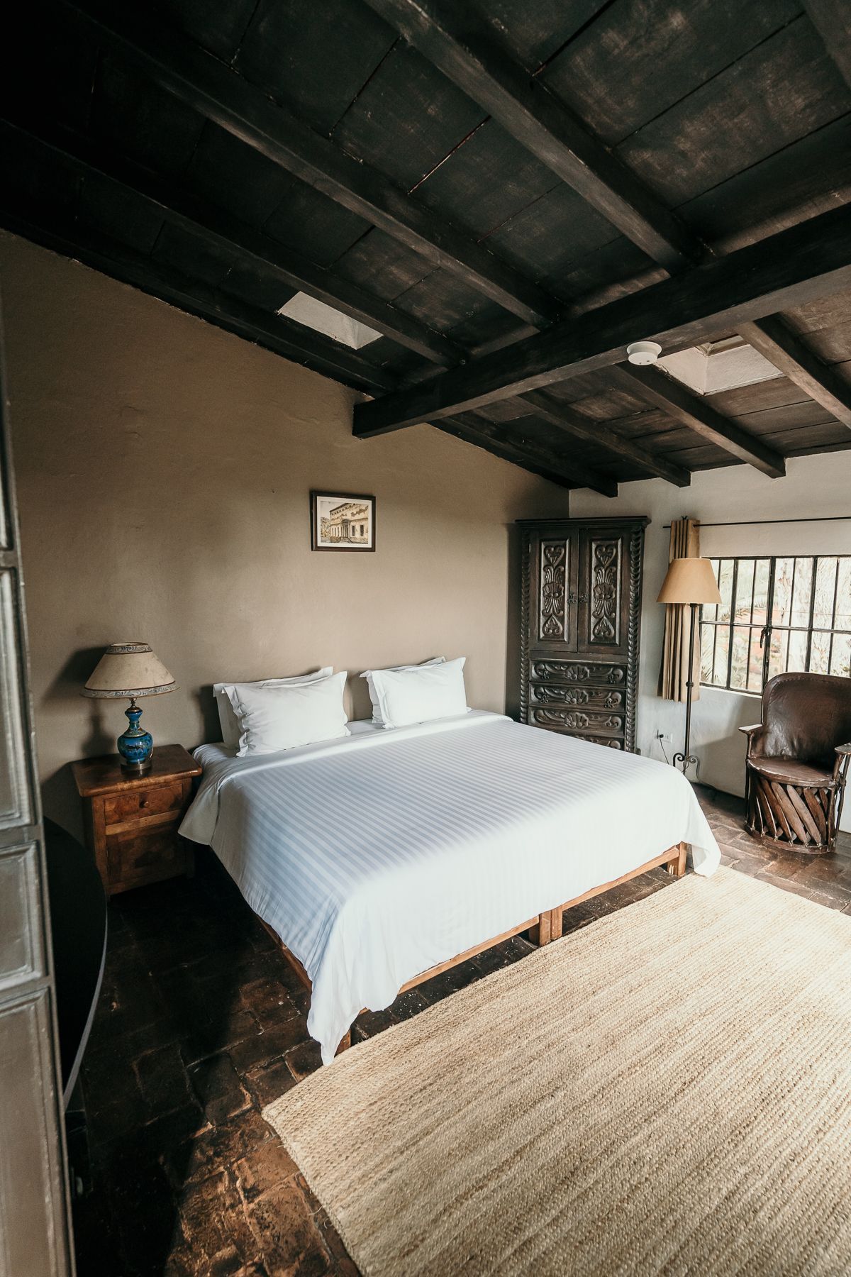 Dormitorio con cama, techo de madera oscura, alfombra y armario. Paredes marrones y luz natural.