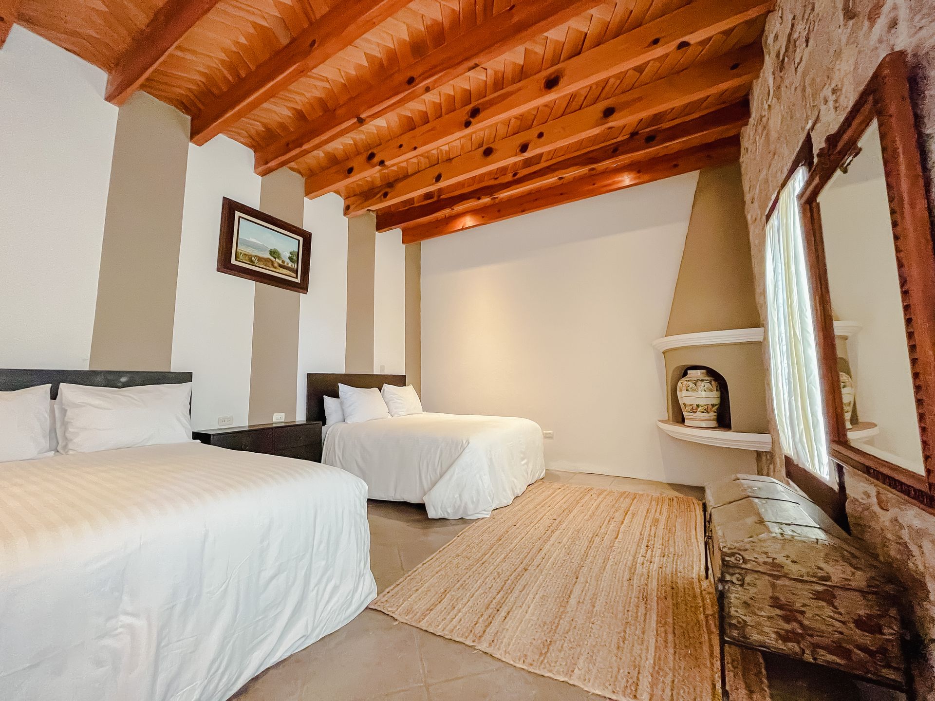 Dormitorio con dos camas, techo de madera a la vista, chimenea de piedra y decoración rústica.