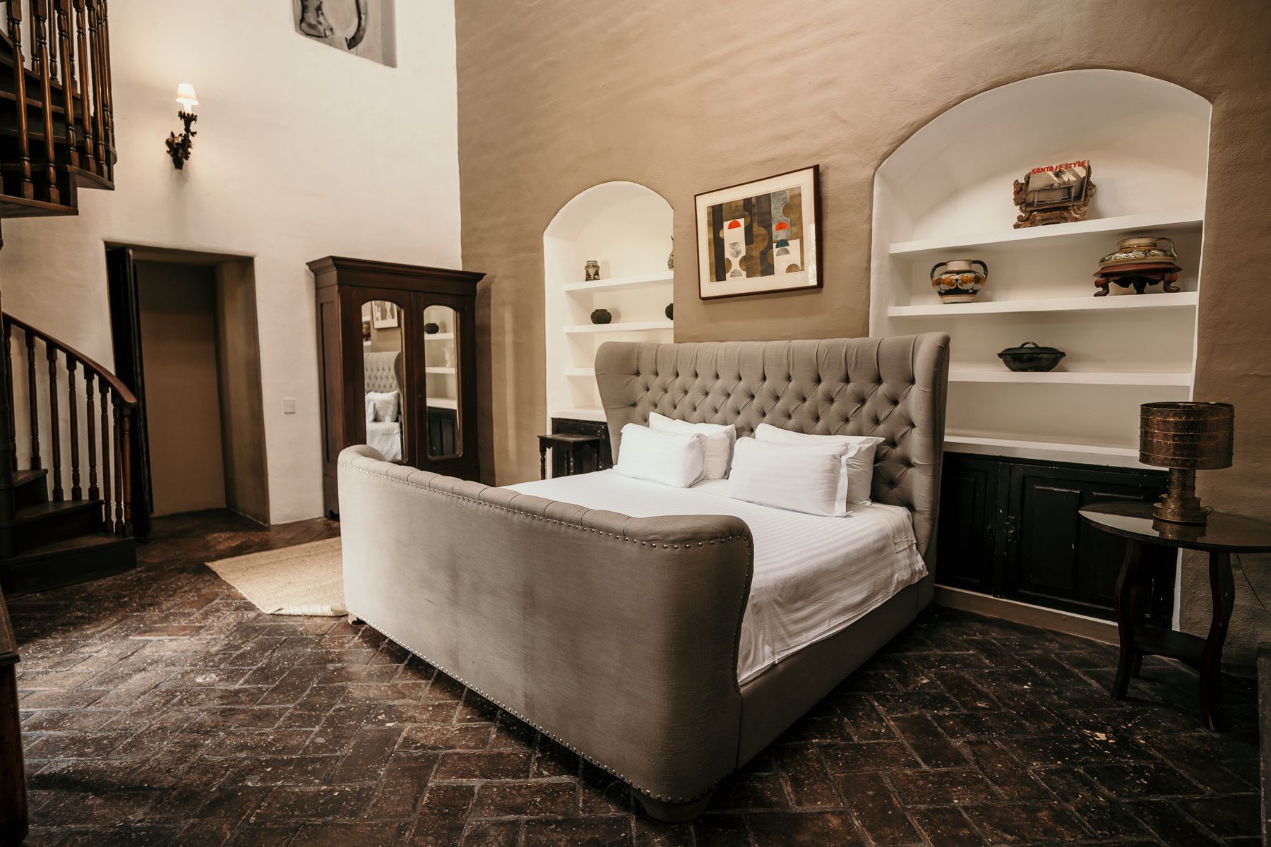Dormitorio con cama grande, estanterías empotradas, muebles antiguos y escalera de caracol. Predominan los tonos tierra.