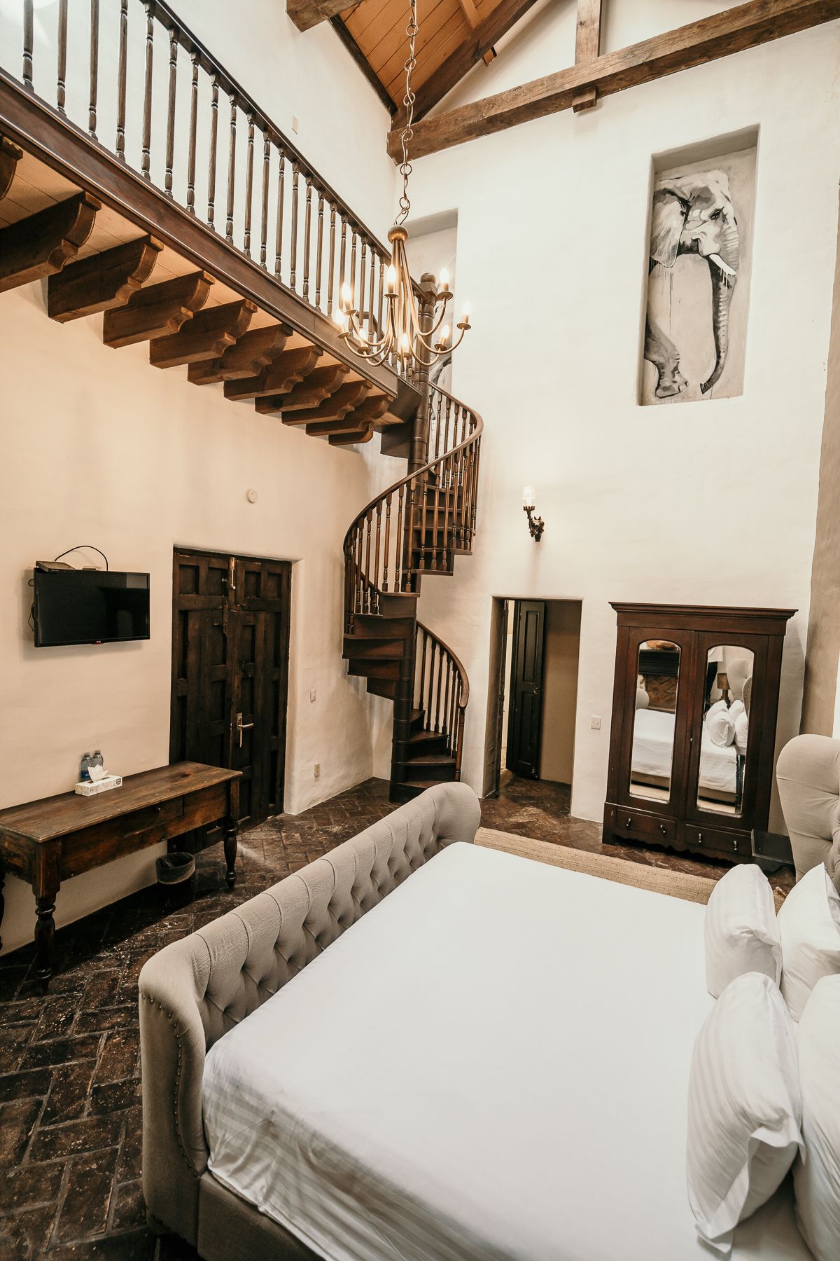 Dormitorio con escalera de caracol, lámpara de araña, detalles de madera y una cama grande.