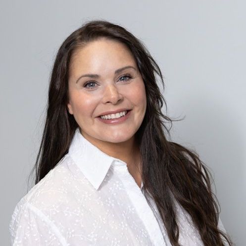 A woman with long hair is wearing a white shirt and smiling.
