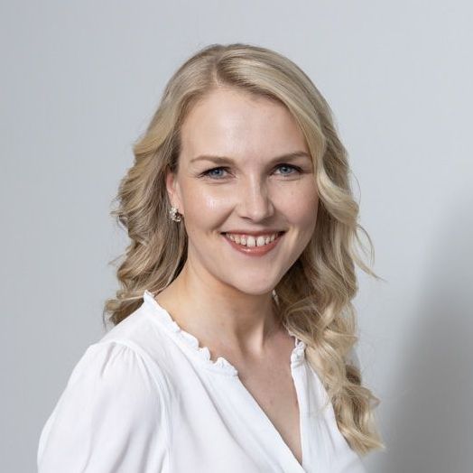A woman with blonde hair is wearing a white shirt and smiling.