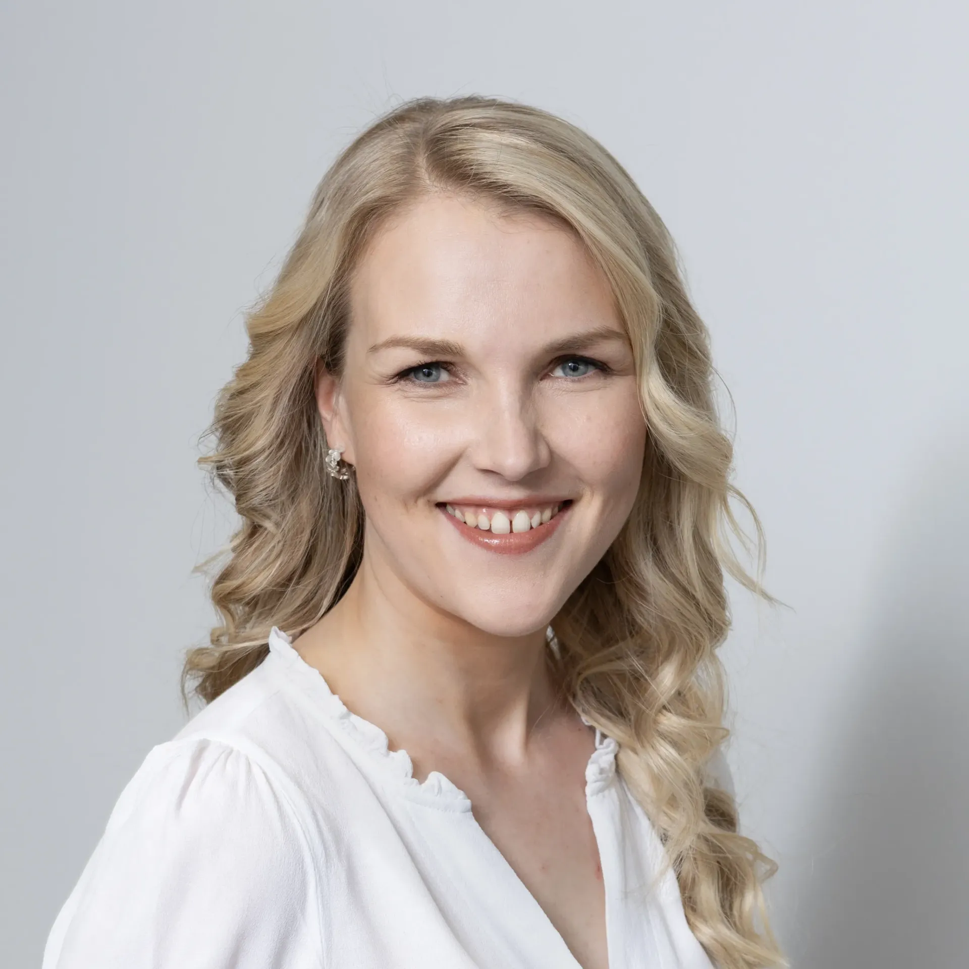 A woman with blonde hair is smiling and wearing a white shirt.