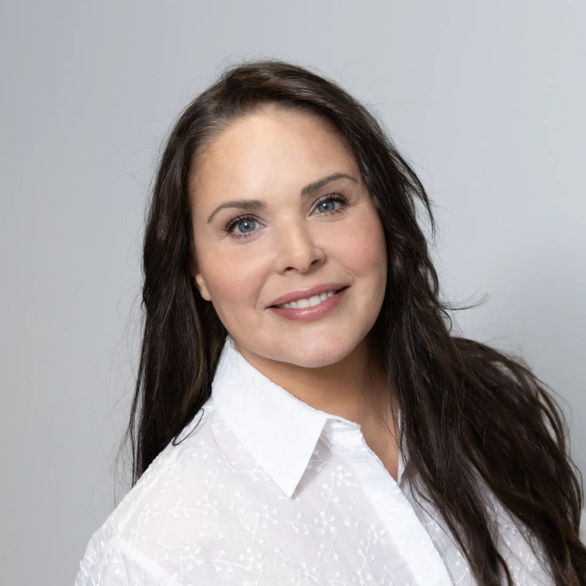 The woman is wearing a white shirt and smiling for the camera.