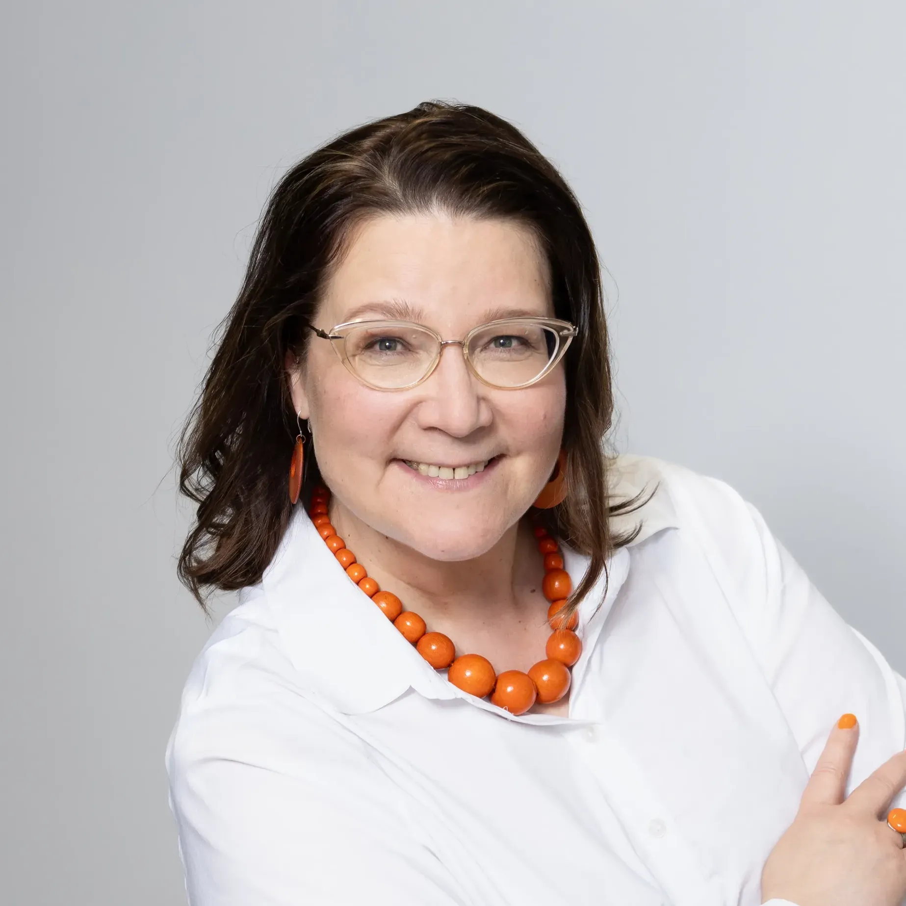 Päivi Saatsi wearing glasses and an orange necklace is smiling for the camera.