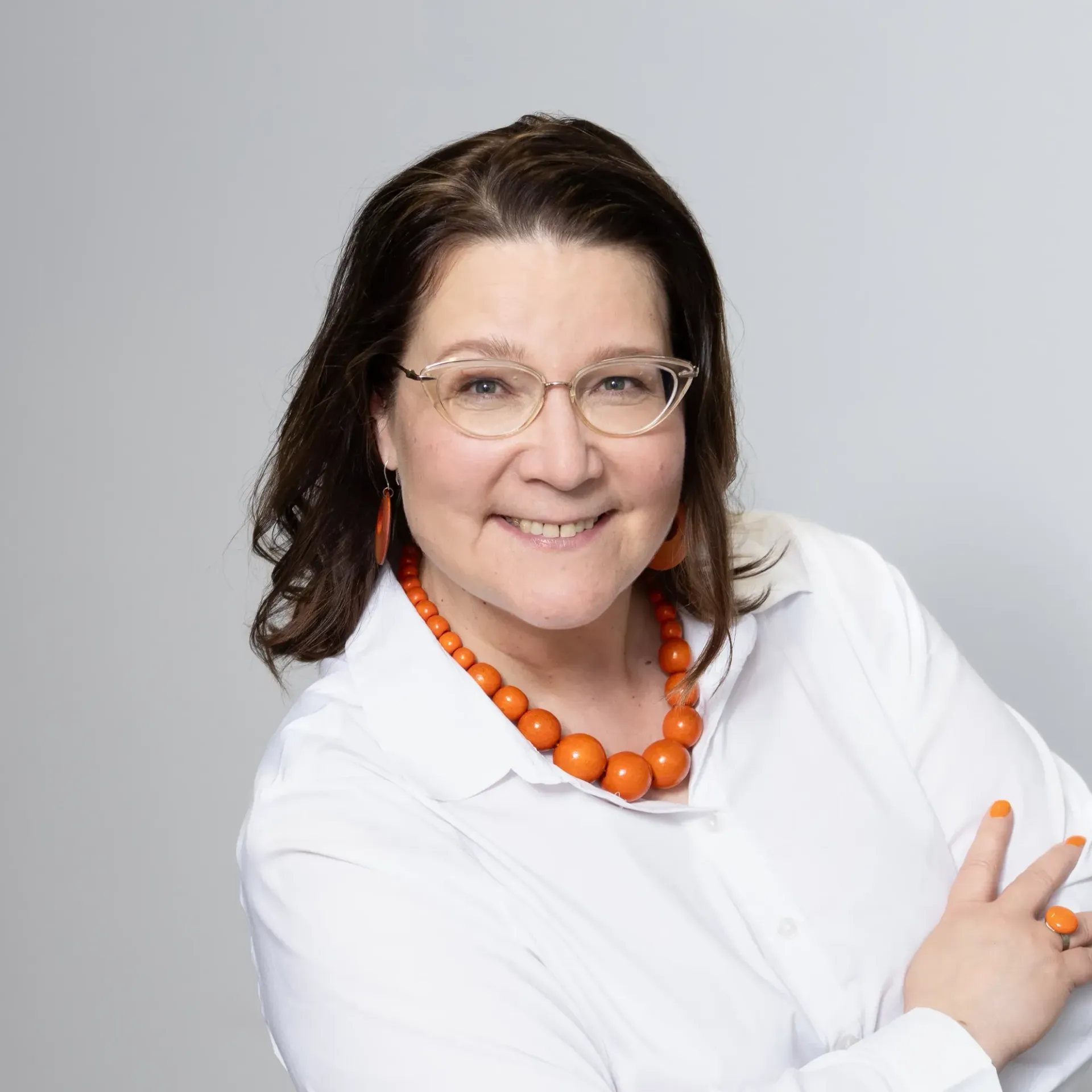 Päivi Saatsi wearing glasses and an orange necklace is smiling for the camera.