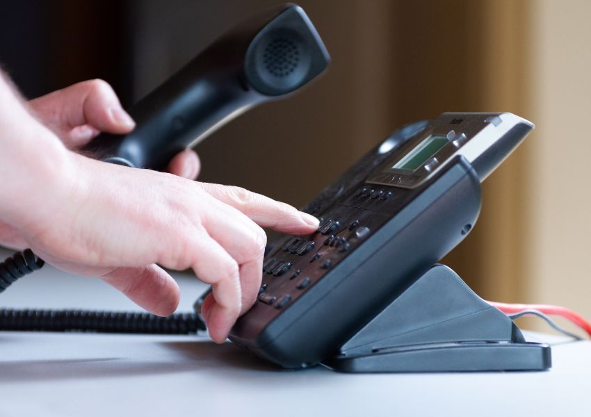 hand dealing on a number on a black land-line phone