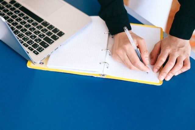 person copying something from laptop into a notebook