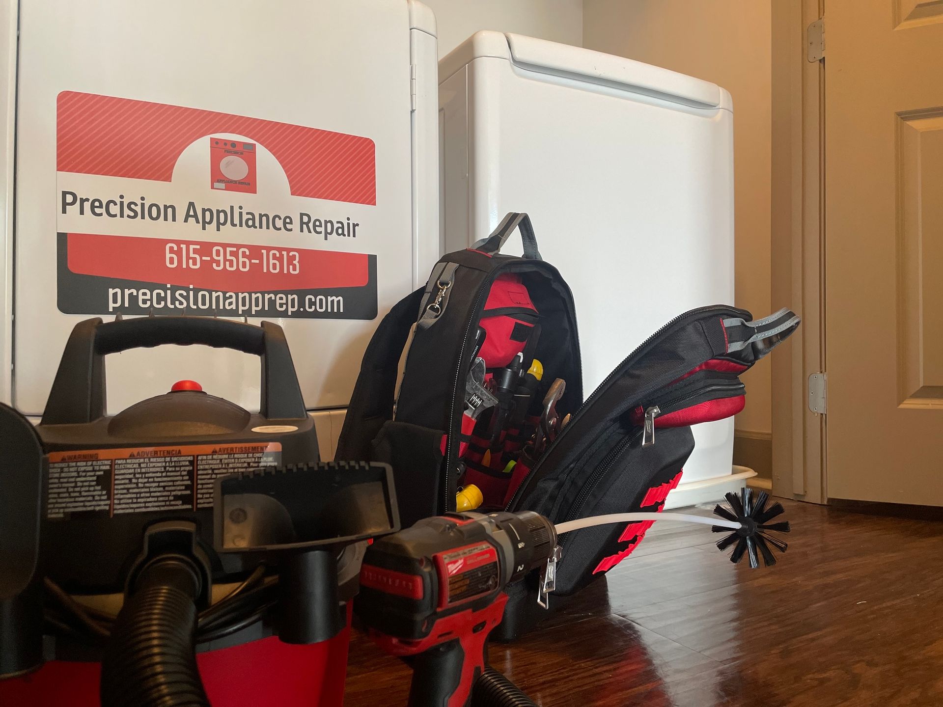 A vacuum cleaner and a drill are on a wooden floor next to a precision appliance repair truck.