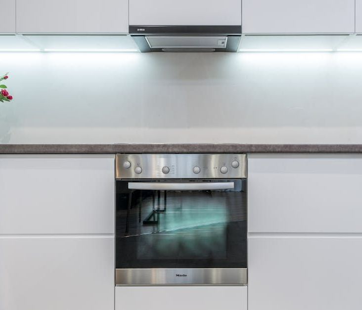 A stainless steel oven is sitting under a hood in a kitchen.