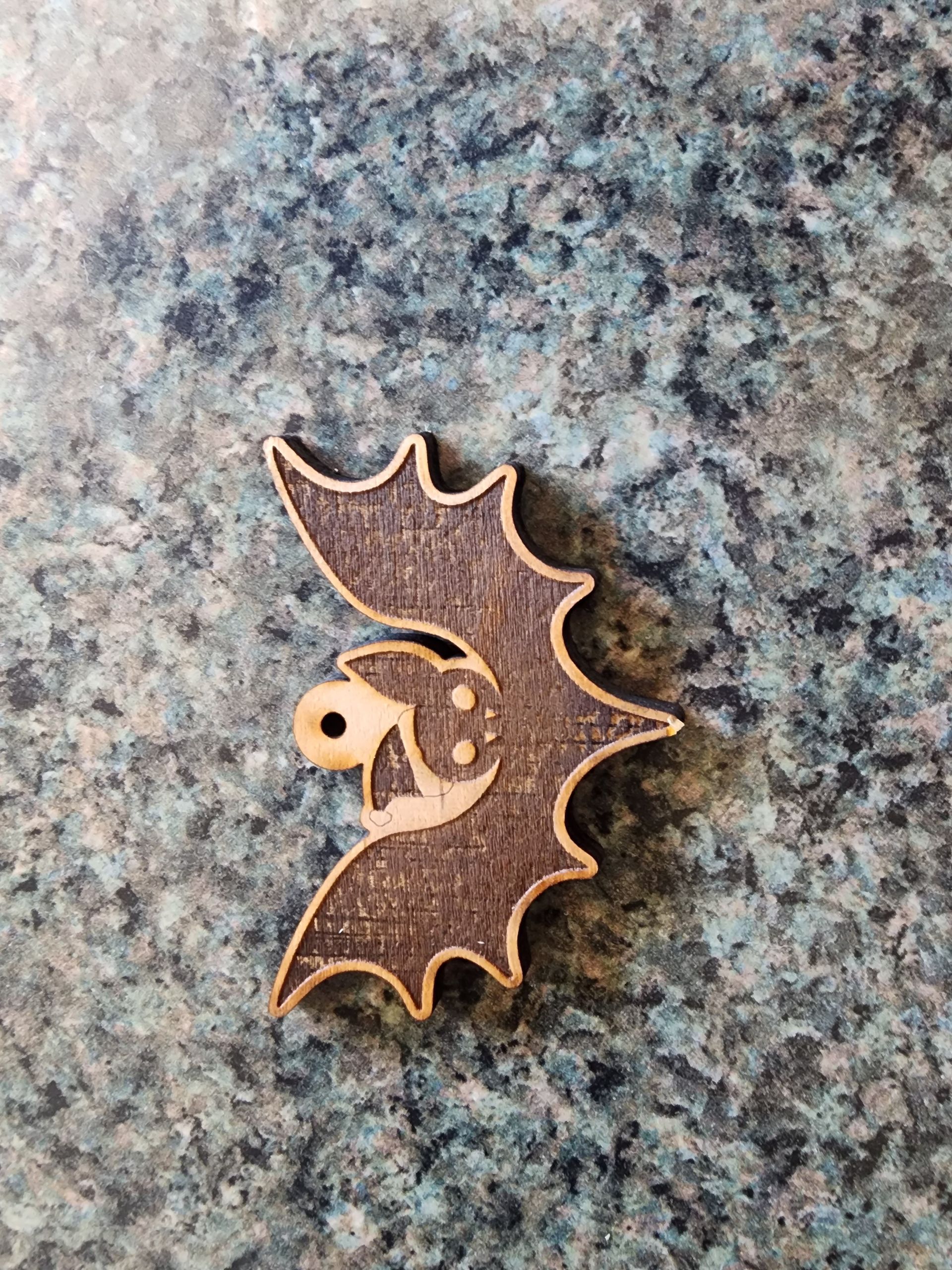 Small wooden bat-shaped pendant with a skull detail on a speckled gray surface