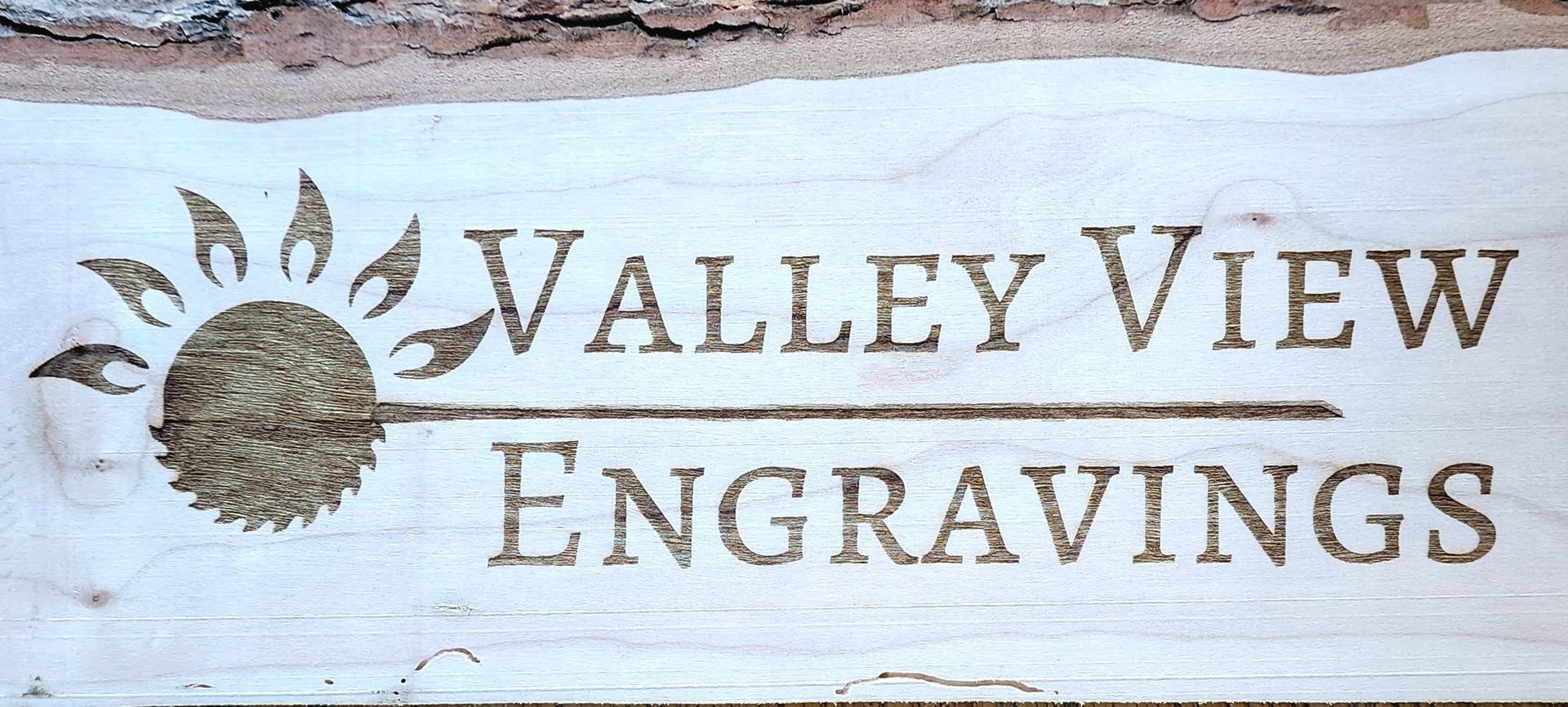 Valley View Engravings logo with sunburst emblem on a light wood sign
