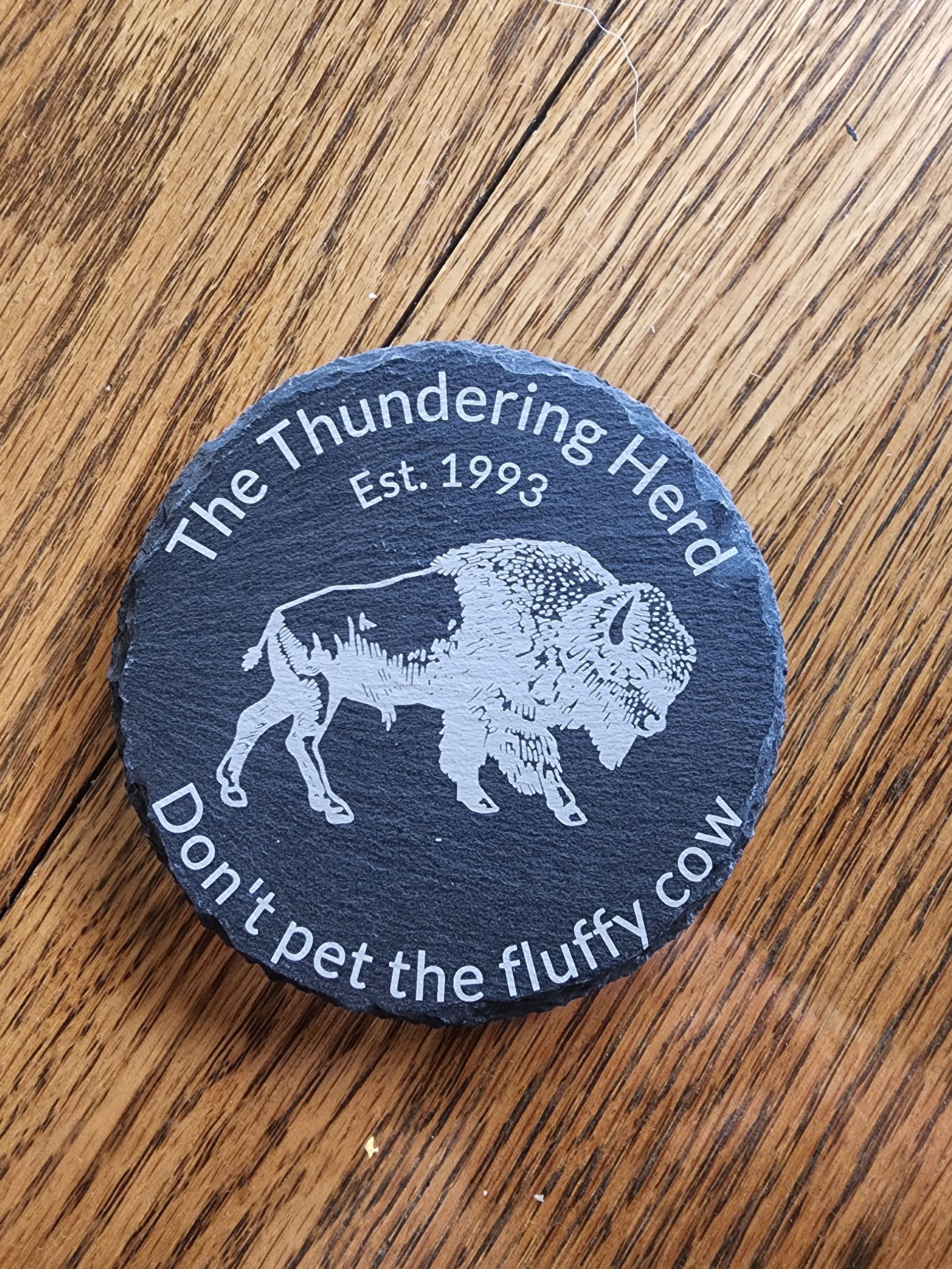 Round black patch on wood table reading “The Thundering Herd Est. 1974” with a bison and calf.