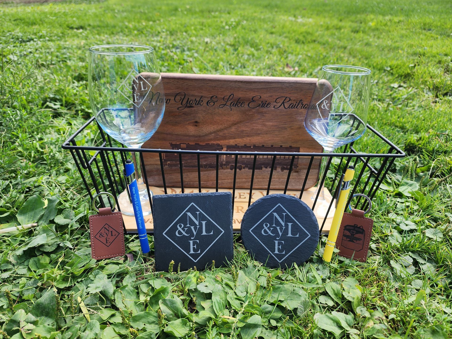Decorative memorial display in a black wire basket on grass with engraved wood and candles.