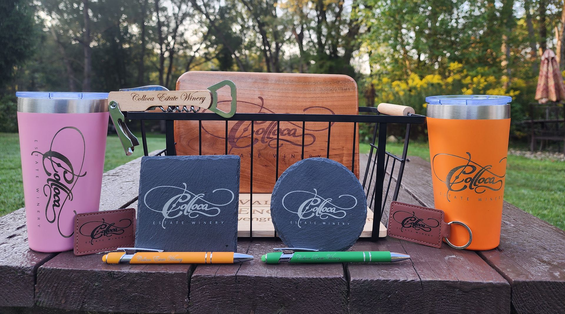 Pink and orange tumblers with branded notebooks and pens on a brick ledge outdoors