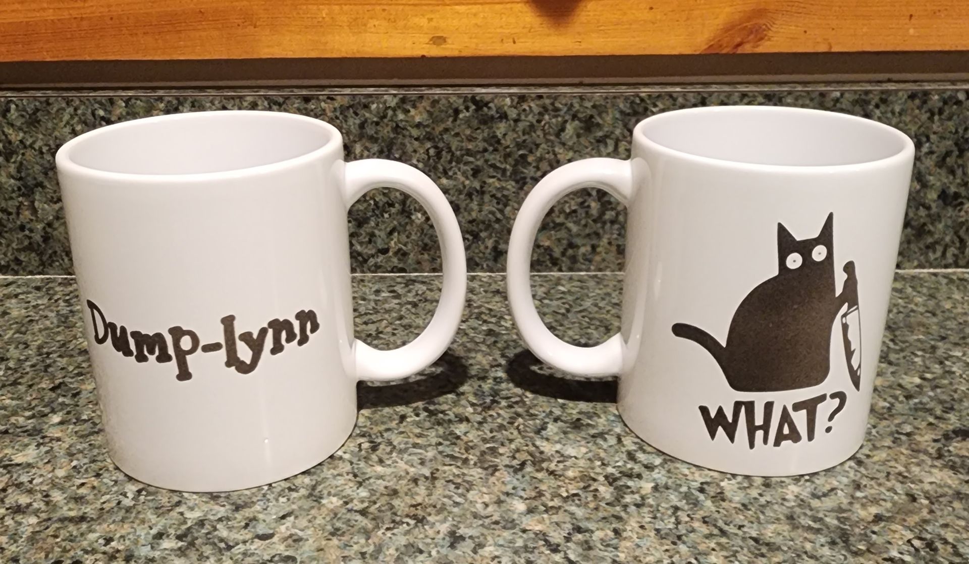 Two white mugs on a countertop; one says 