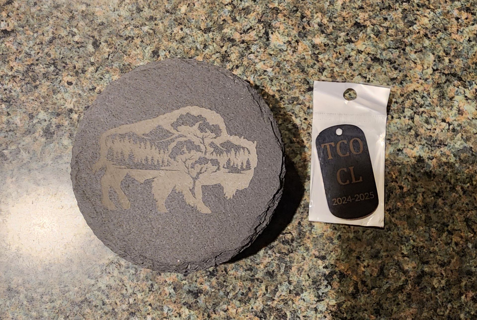 Gray round stone with engraved animal design beside a small black-and-white tag on a granite countertop