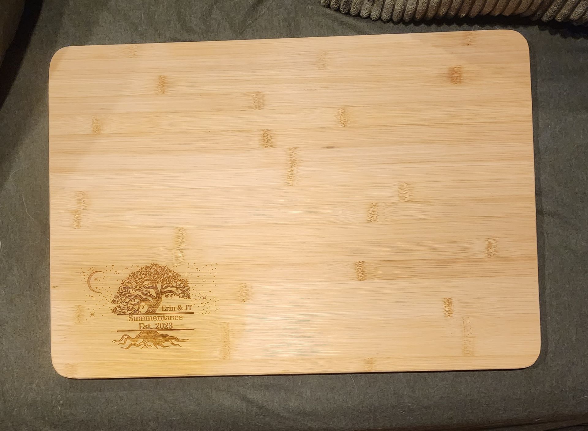 Light wooden cutting board with a small dark stain on the lower left, on a gray fabric surface