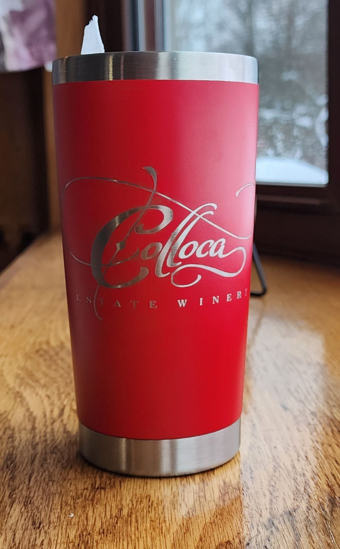 Red Coca-Cola insulated tumbler on a wooden table near a window.