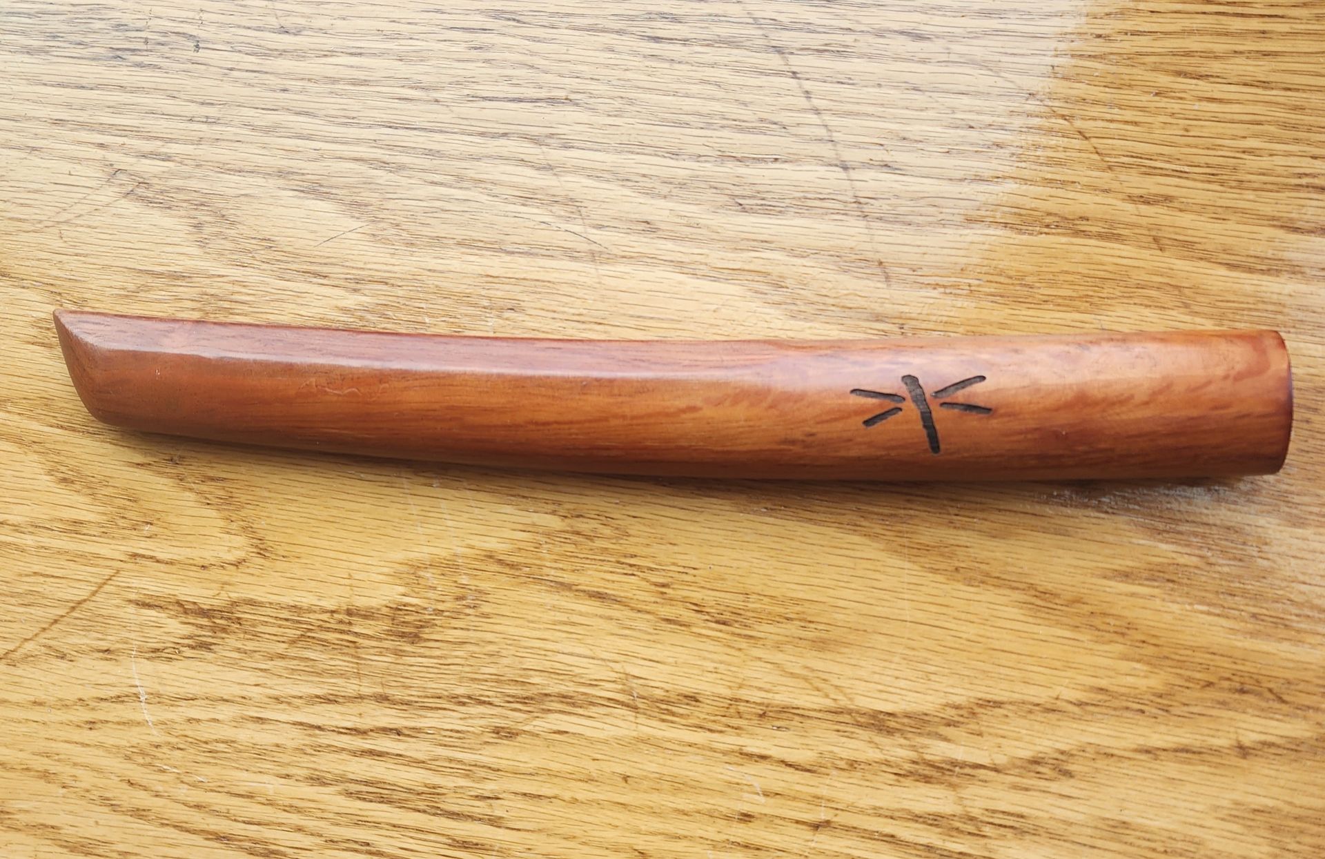 Small curved wooden object with a carved insect-like symbol on a wood-grain surface