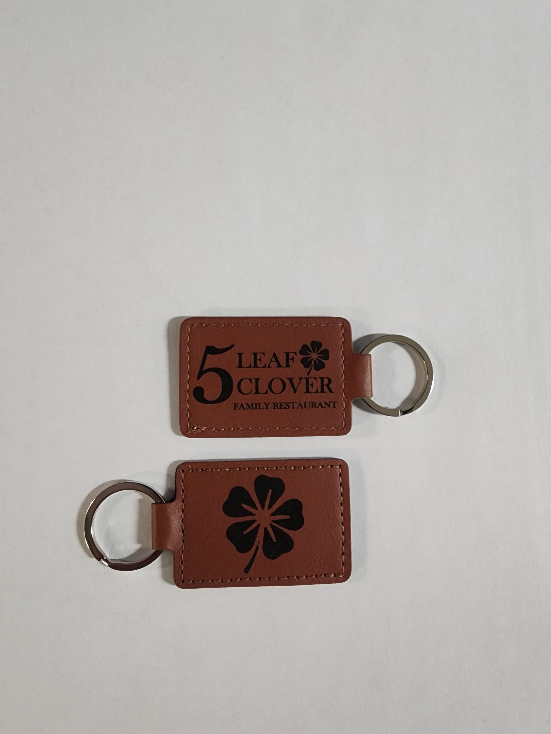 Two brown leather key tags with silver rings, one printed “5CLOVER” and one with a black clover logo.