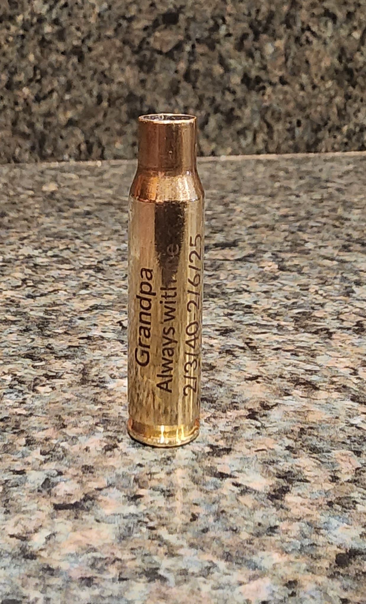 Gold brass cartridge-shaped candle holder on a speckled granite countertop, against a granite backsplash.