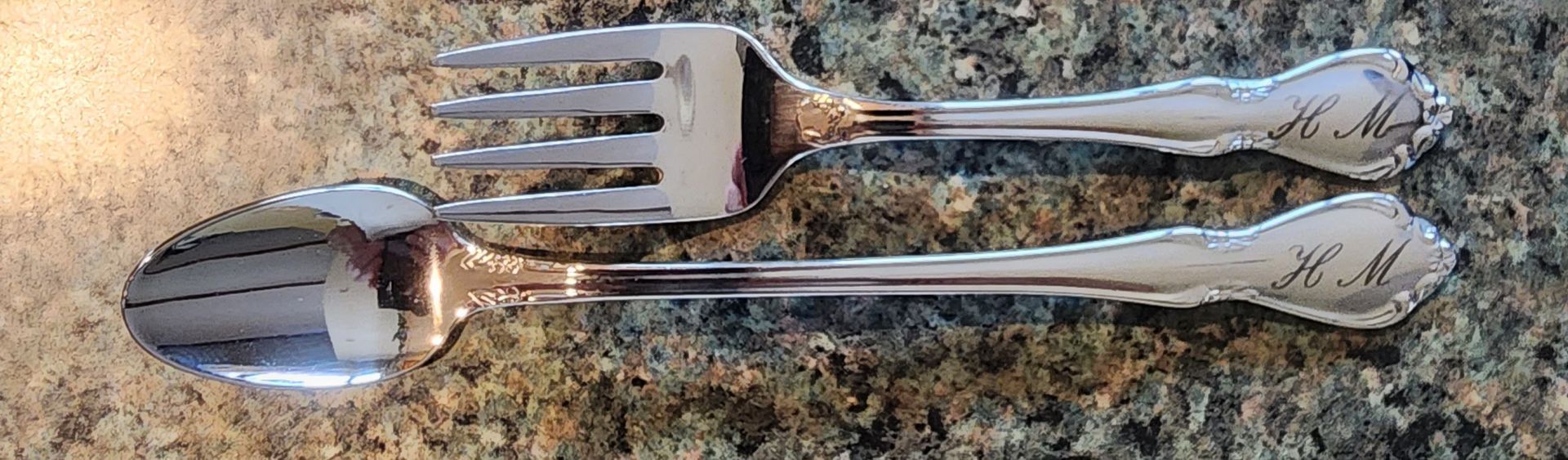 Two silver utensils, a fork and spoon, resting on a speckled countertop.