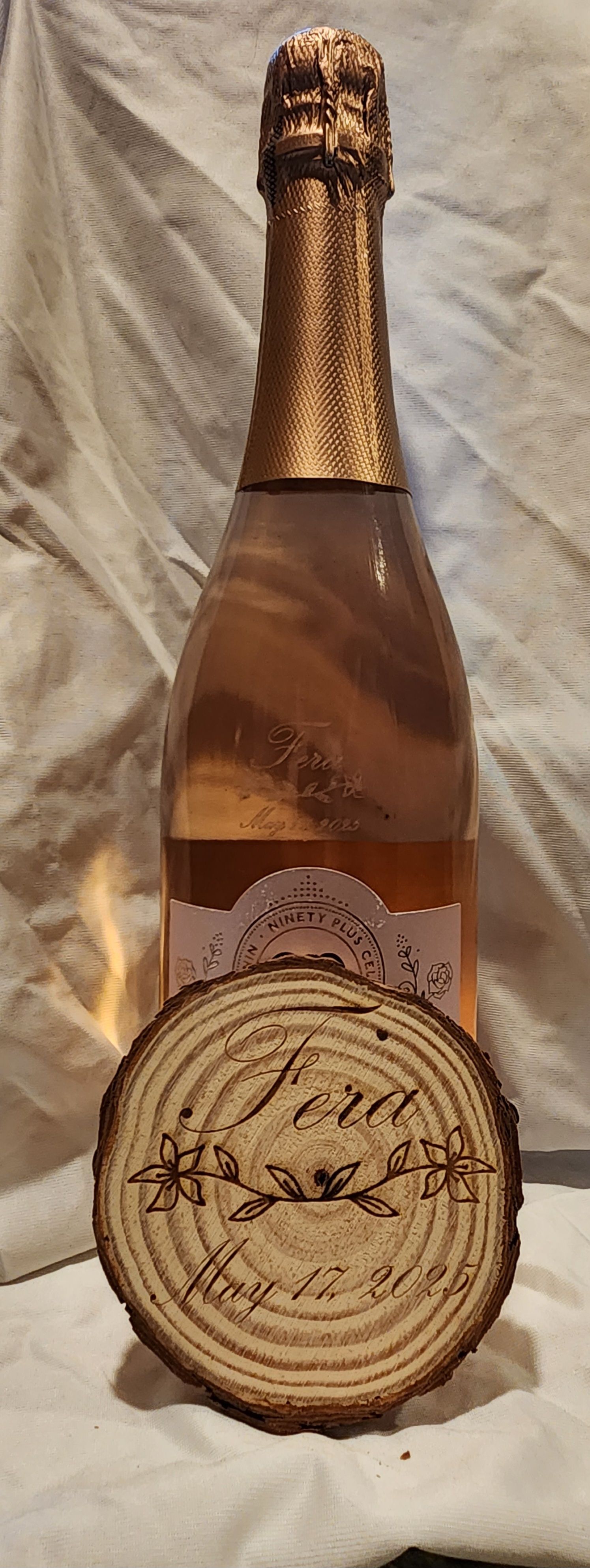 Bottle of sparkling rosé with gold foil neck and round beige label on a soft fabric background