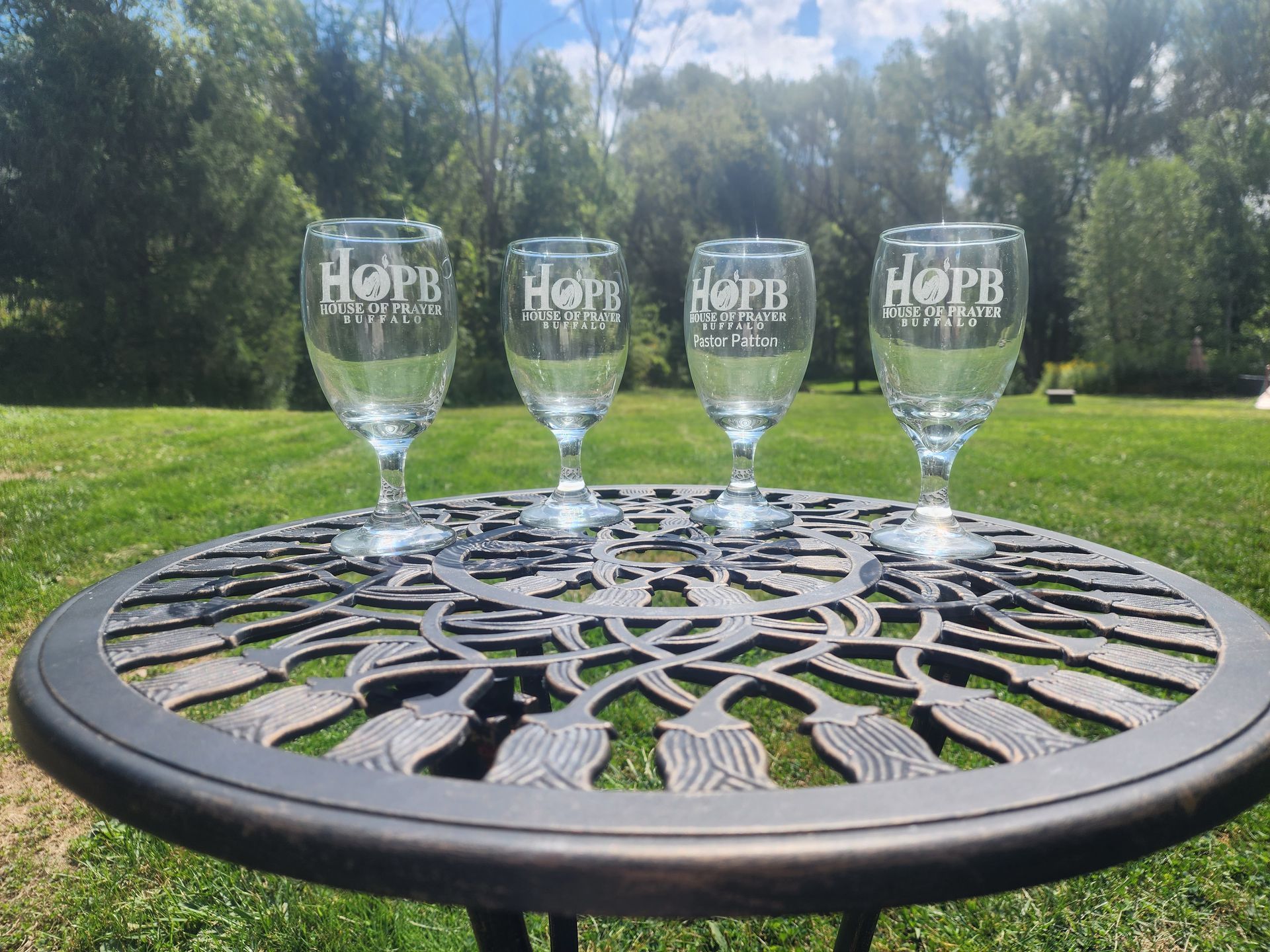 Four clear beer glasses on a black patio table in a sunny grassy yard