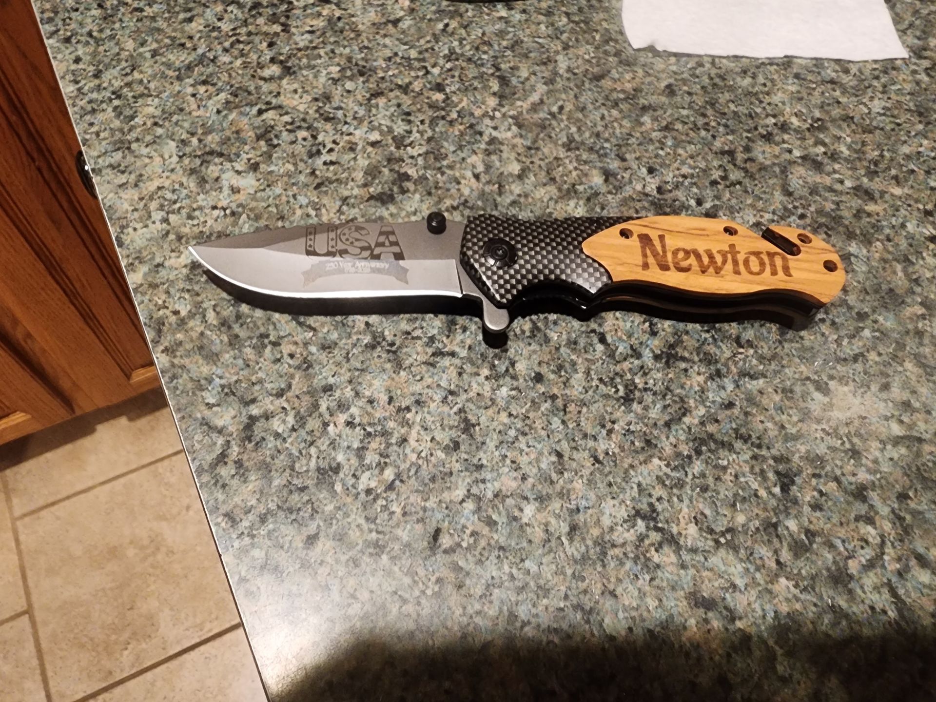 Open folding knife with wooden handle engraved “Newton” on a granite countertop.