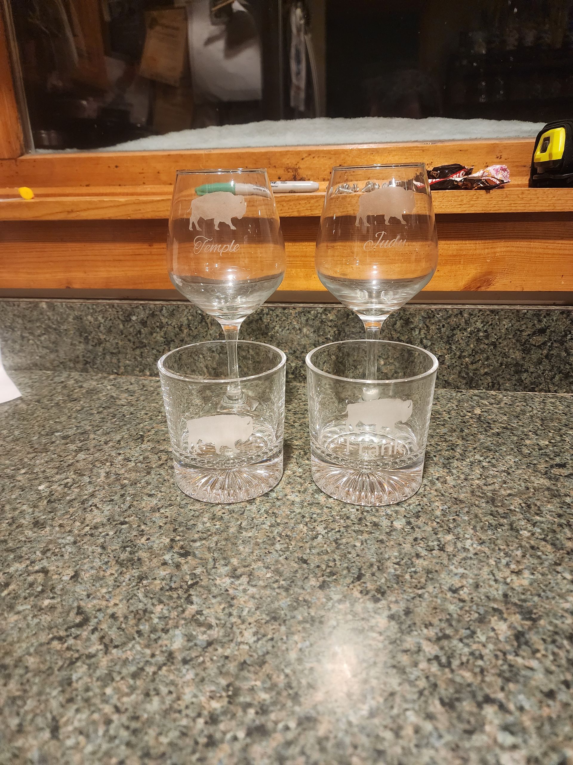 Two empty wine glasses balanced on two clear tumblers on a speckled countertop.